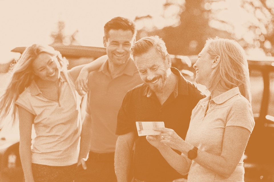 Four adults stand outdoors by cars in Medina Valley, smiling and looking at a piece of paper held by one woman. The scene appears friendly and informal, suggesting excitement about new homes for sale in Briggs Ranch.