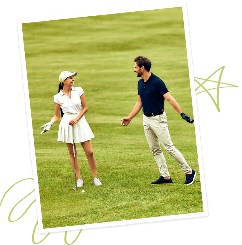A woman and a man stand on the lush golf course at Briggs Ranch, talking and smiling. The woman holds a golf club, dressed in a white outfit and cap; the man wears a navy polo and beige pants in this master-planned community.