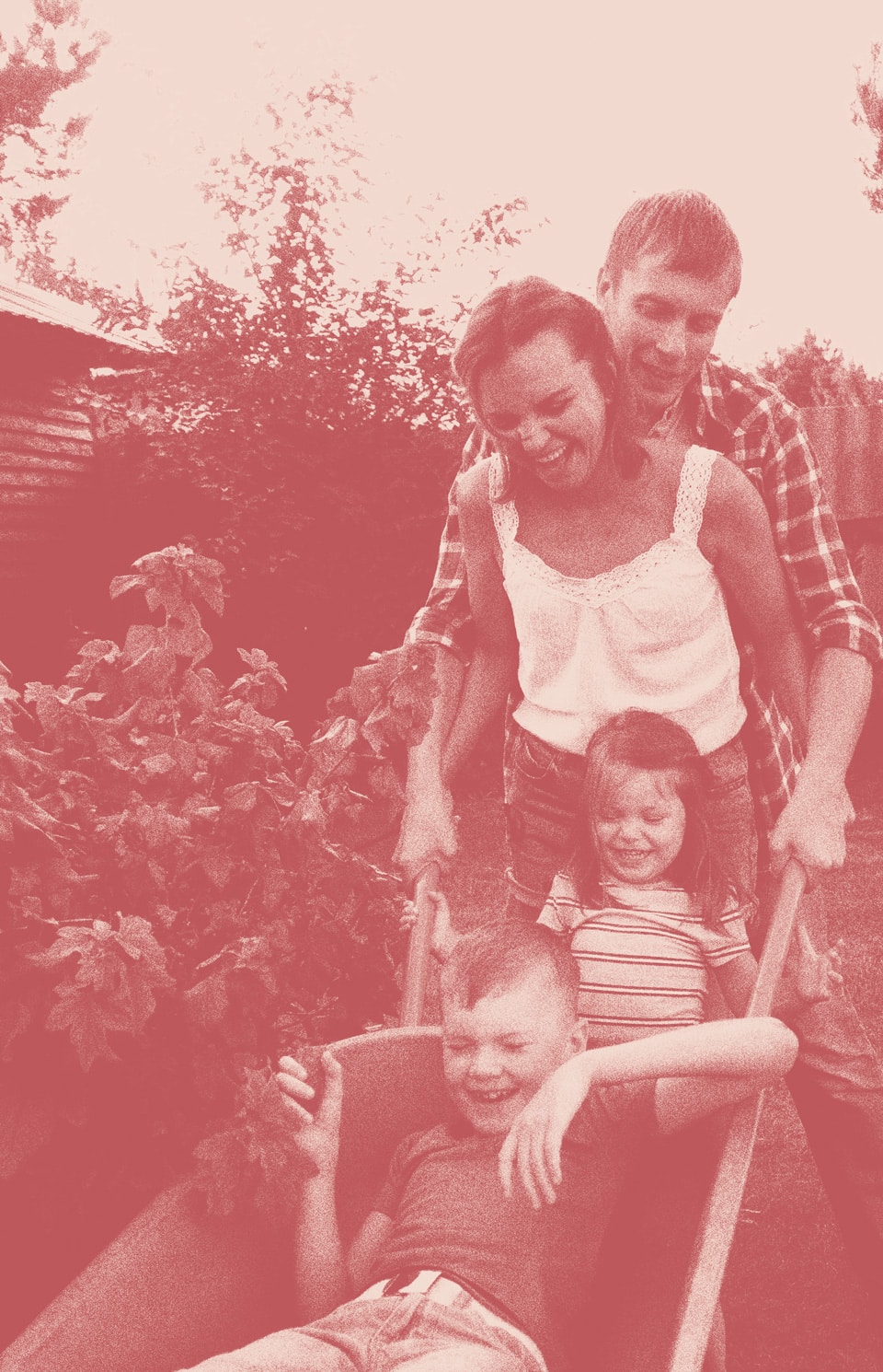 Two adults push a wheelbarrow with two smiling children seated inside, enjoying a playful moment together outdoors near bushes—capturing the joy of family in Medina Valley, where new homes for sale offer space to create memories like these.