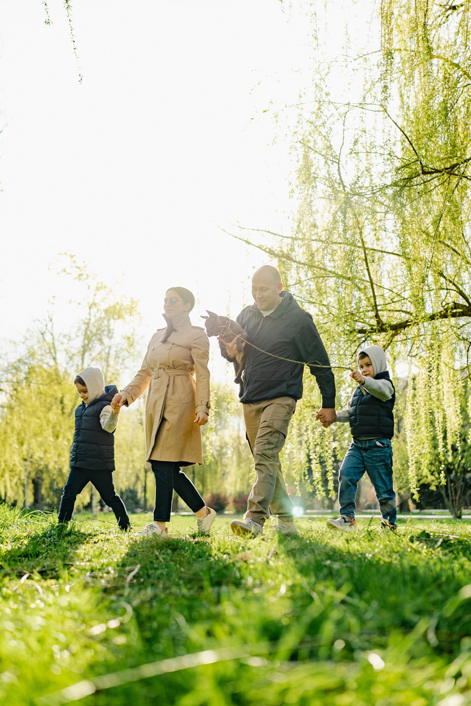 A family of four, with two adults and two children, walks together in a grassy park on a sunny day in a master-planned community featuring new homes for sale in San Antonio.