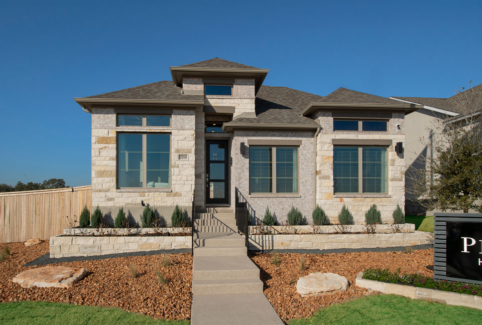 Modern single-story stone house in Briggs Ranch with large windows, a central front door, neatly landscaped yard, and a small staircase leading to the entrance—your ideal spot among new homes for sale in Medina Valley.