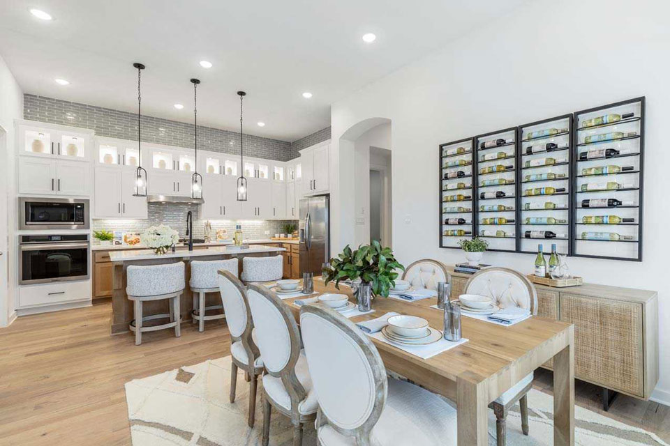 Modern open-concept kitchen and dining area with white cabinets, a large island, pendant lights, and a wall-mounted wine rack—perfect for entertaining in new homes for sale in Medina Valley, San Antonio.