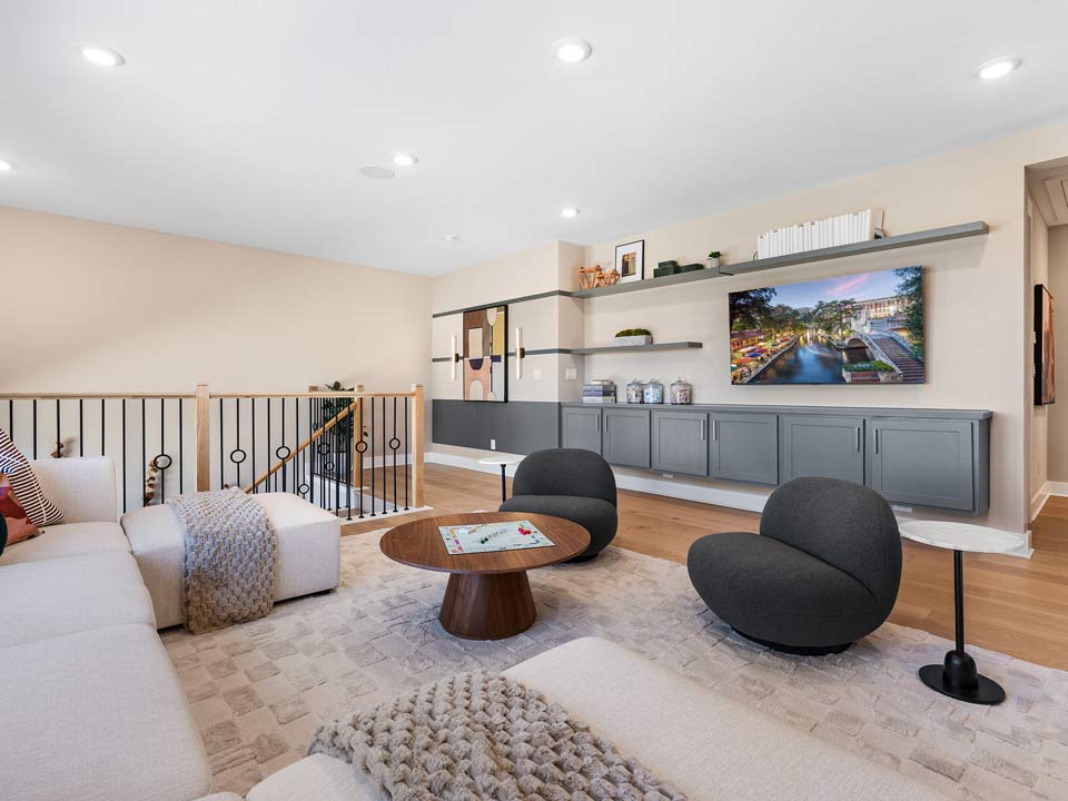 Modern living room with beige walls, a large white sectional sofa, two dark round chairs, and a wooden coffee table—perfect for relaxing in one of Medina Valley’s beautiful master-planned communities with new homes for sale.