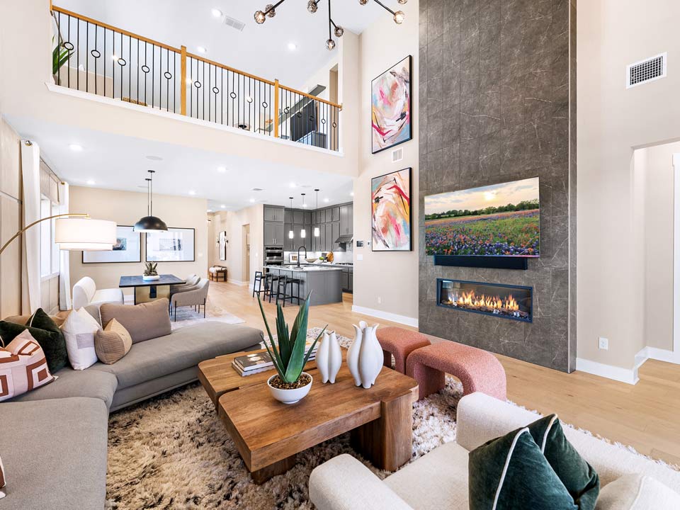 Modern open-concept living room in one of Medina Valley's new homes, featuring a sectional sofa, wooden coffee table, fireplace, wall-mounted TV, high ceilings, and balcony railing with views into the kitchen and dining area.