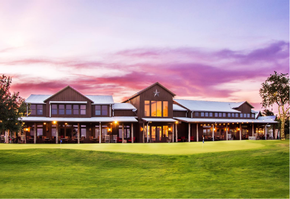 A large ranch-style building with a covered porch sits on a manicured lawn under a pink and purple sunset sky, showcasing the charm of new homes for sale in San Antonio.