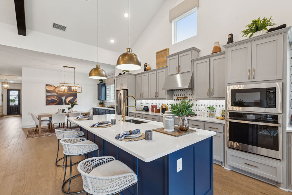 Modern kitchen with gray cabinets, a large island with bar stools, stainless steel appliances, pendant lights, and an adjacent dining area in one of the stunning new homes for sale in Medina Valley.