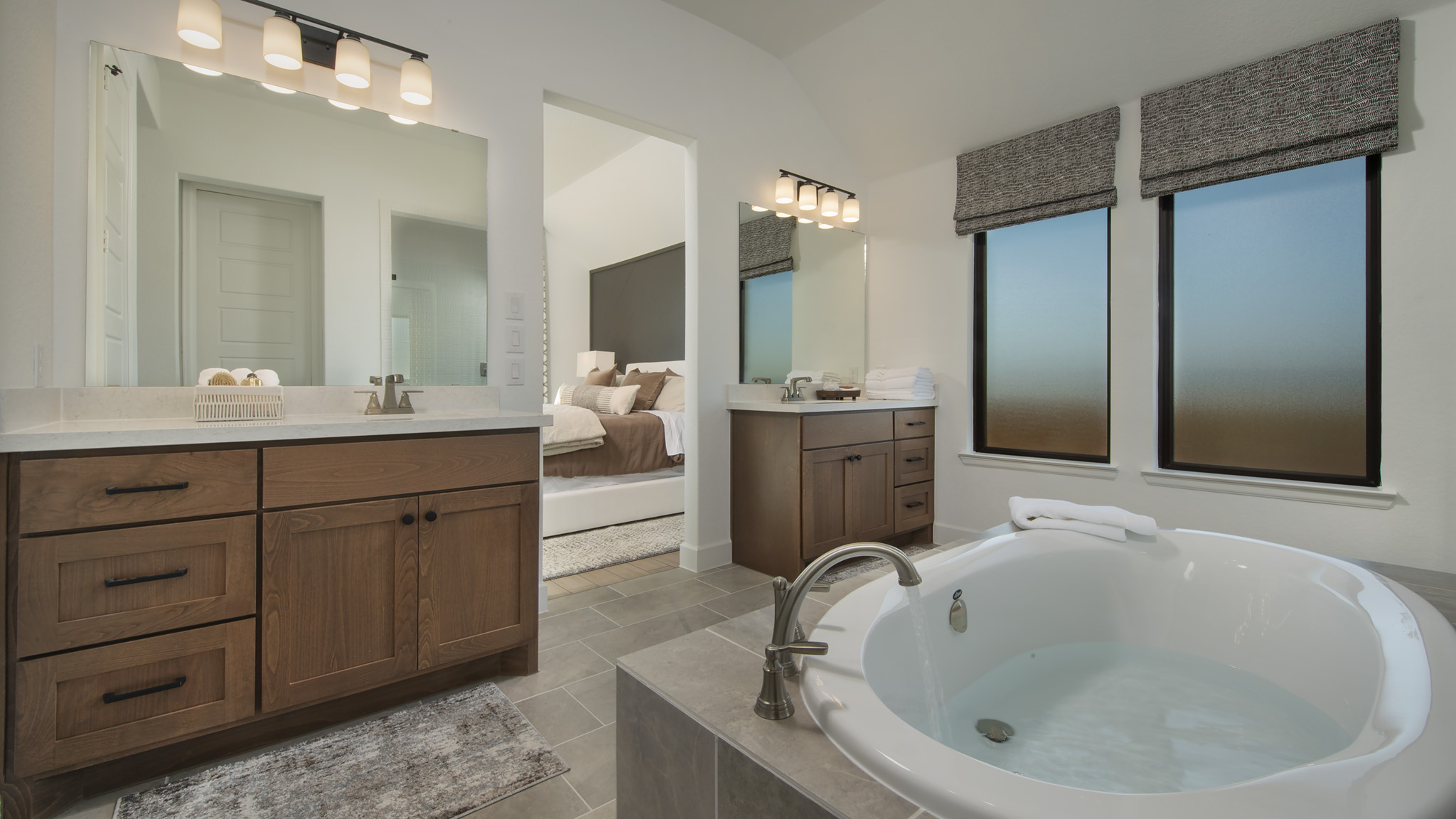 Modern bathroom with soaking tub, double vanities, and view into a bedroom.