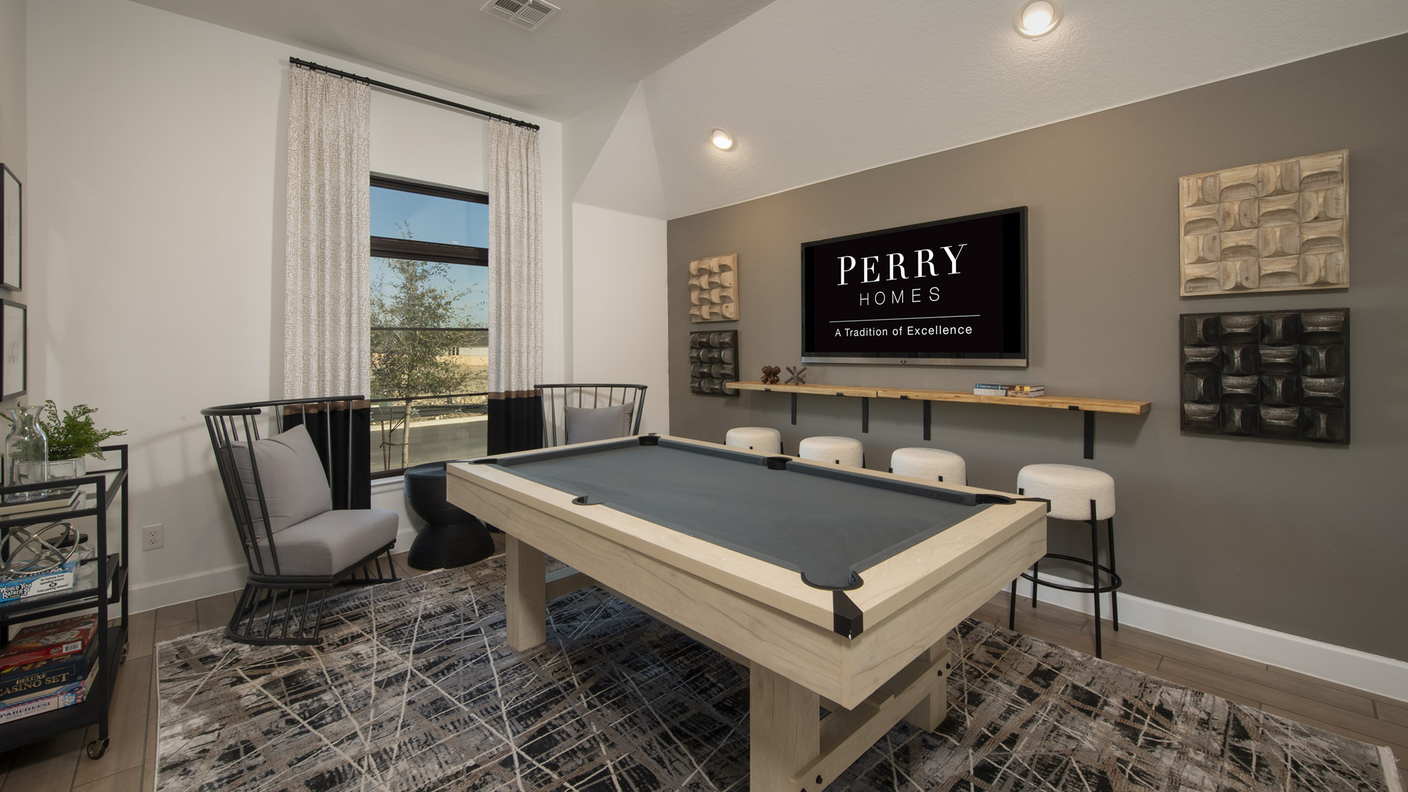 Modern game room with a pool table, chairs, wall art, and a TV displaying Perry Homes.