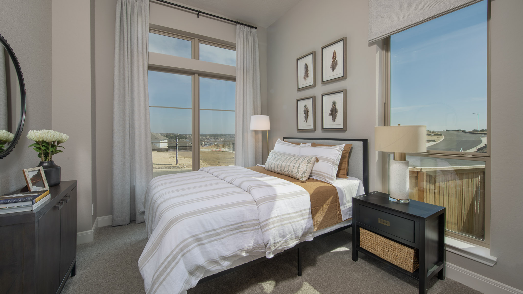 Bright bedroom with large windows, a bed, two nightstands, and framed art on the wall.