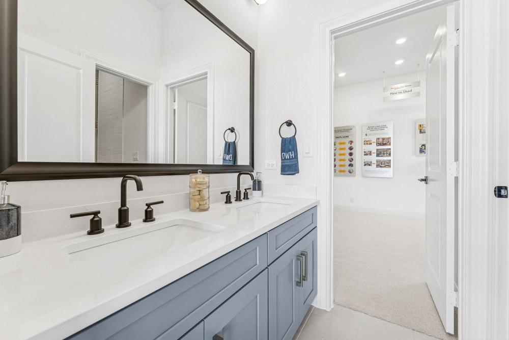 Modern bathroom with double sink vanity, large mirror, and view into a carpeted hallway.
