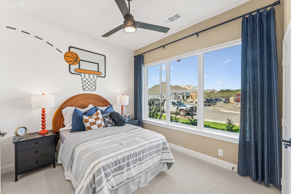 Bedroom with basketball-themed wall art, bed, nightstands, and large window showing street view.