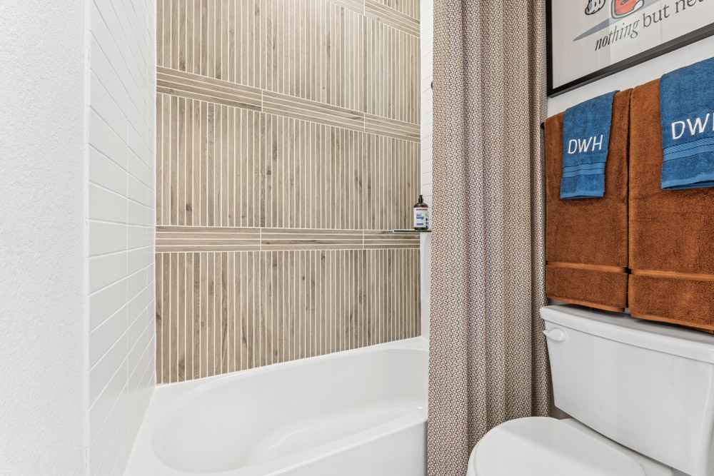 Modern bathroom with a white bathtub, tan tile wall, and towels on a rack above the toilet.
