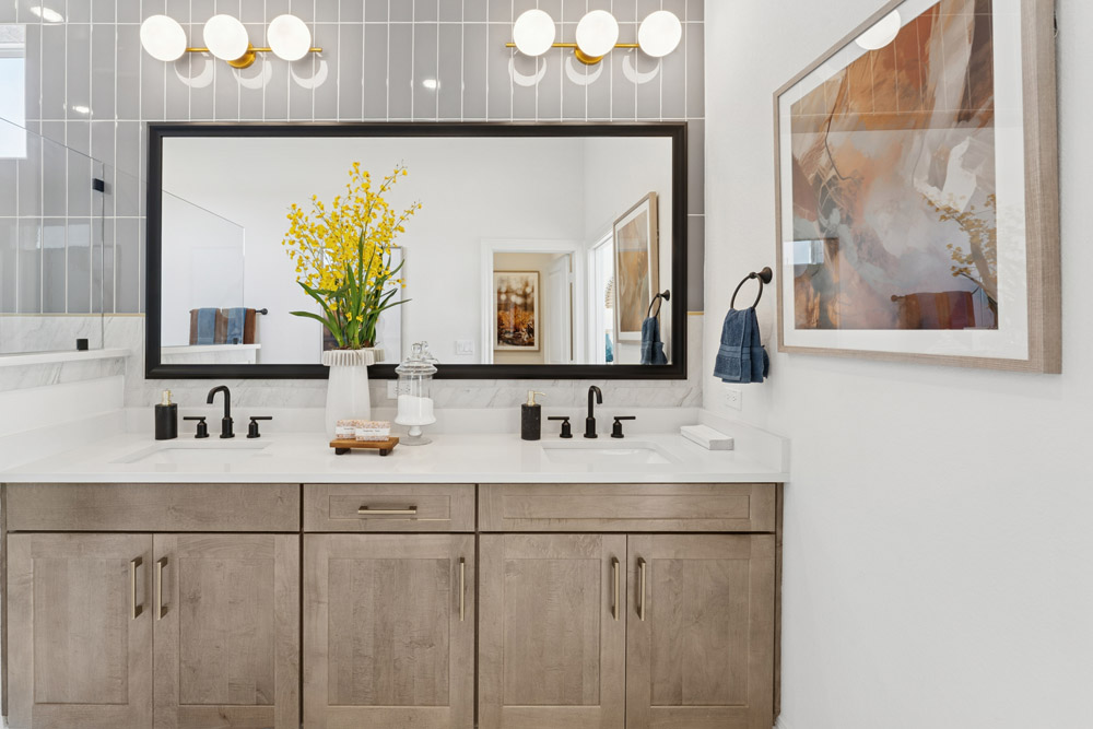 Modern bathroom with double sinks, large mirror, wood cabinets, and decorative yellow flowers.
