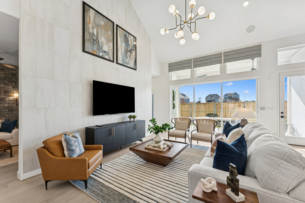 Modern living room with large windows, neutral decor, and a wall-mounted TV.