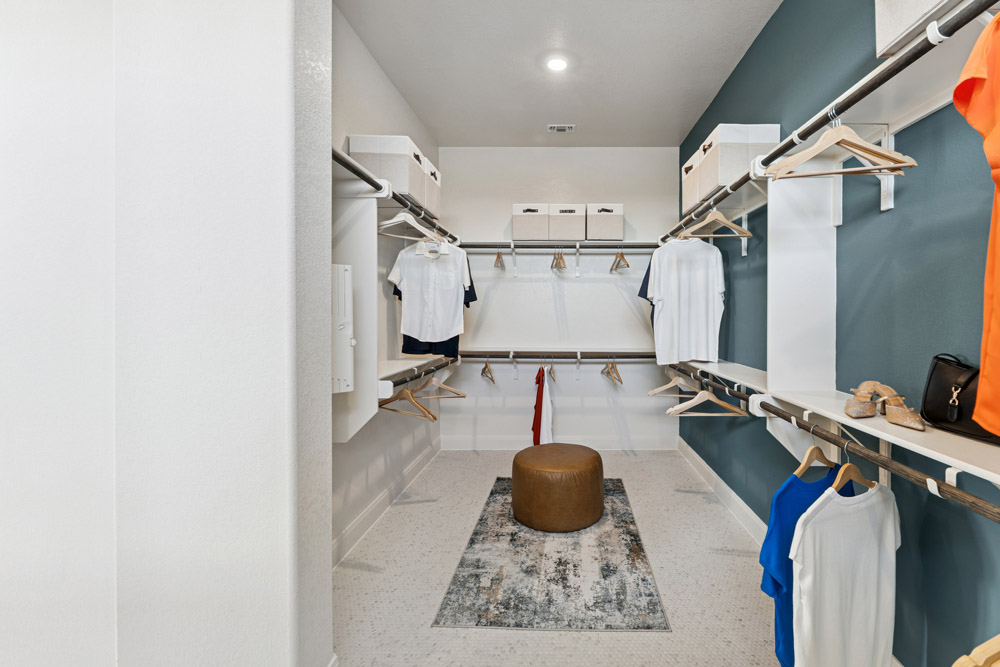 Spacious walk-in closet with clothes on racks, shelves, a rug, and a round ottoman.