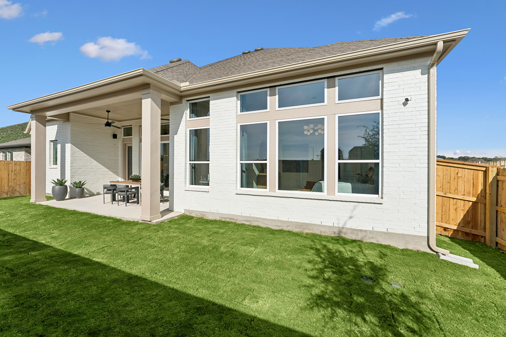 Back view of a modern house with large windows and a covered patio facing a grassy yard.
