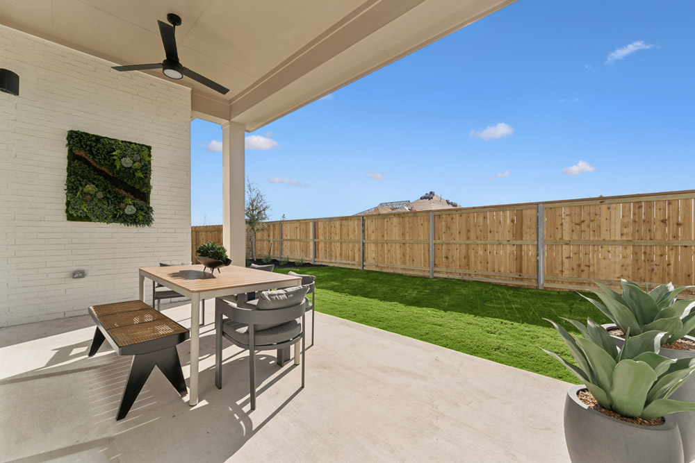 Covered patio with dining table, chairs, bench, potted plants, and fenced backyard.