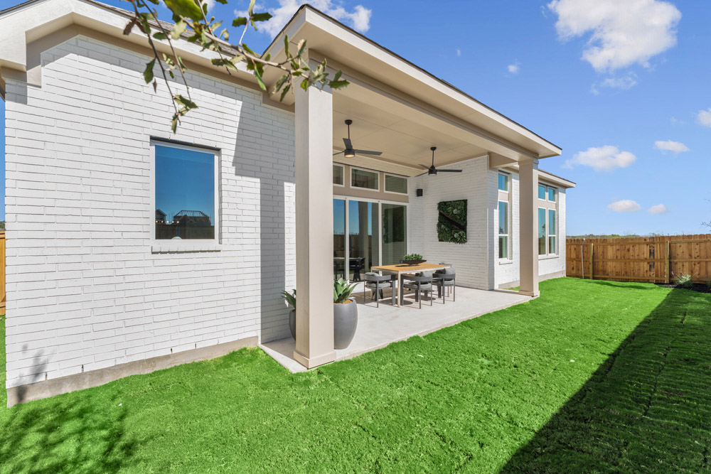 Modern white brick house with covered patio, outdoor dining set, and artificial grass lawn.