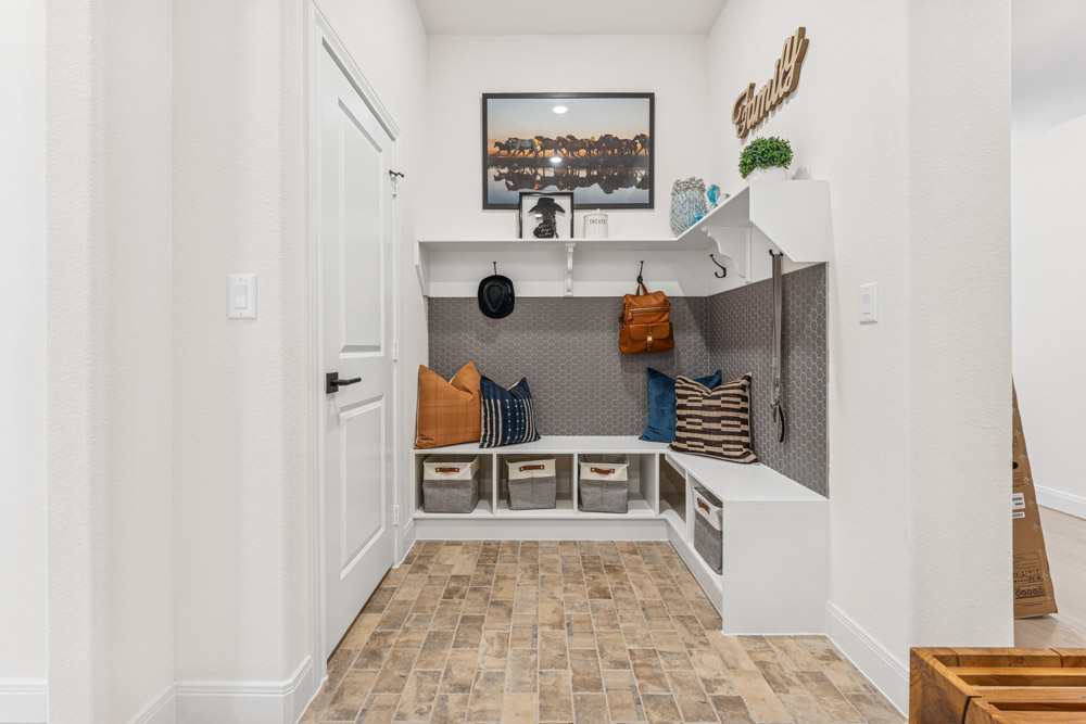 A mudroom with storage benches, bins, hooks, pillows, and a framed photo on the wall.