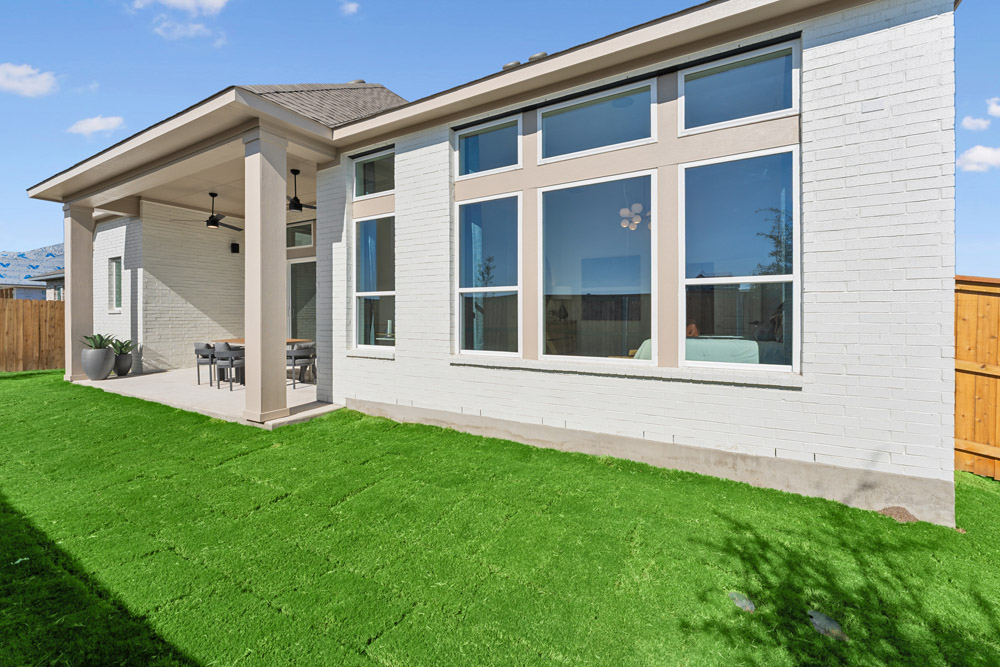 Modern white brick house with large windows and covered patio overlooking a green lawn.