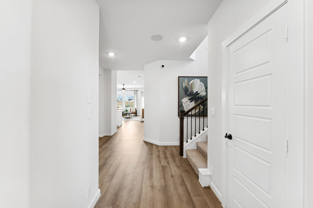 Entry hallway with wood flooring, white walls, a staircase, and view into a living area.