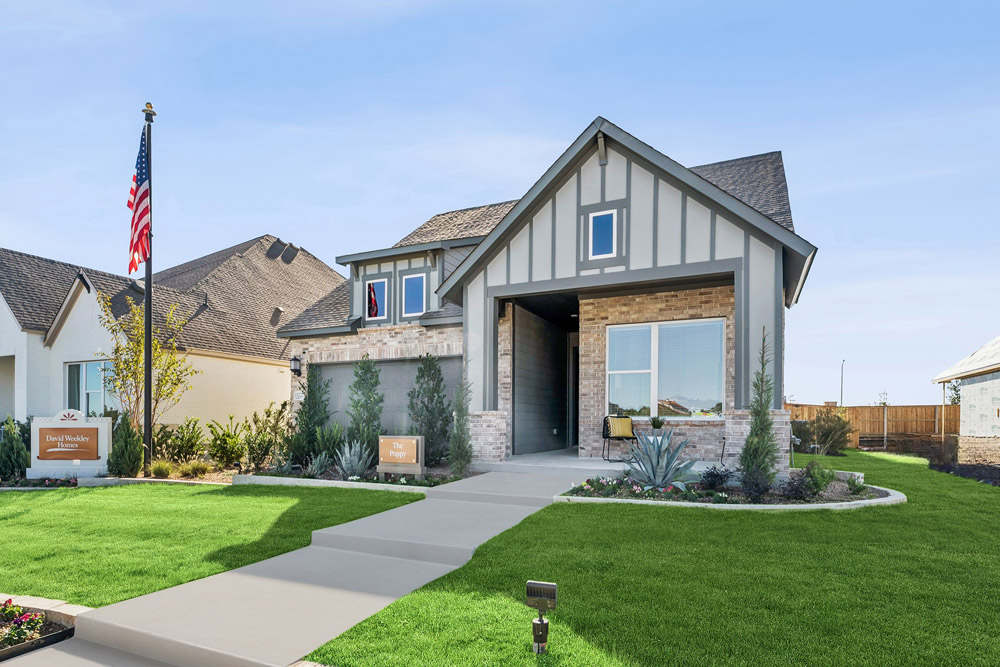 Modern suburban house with a manicured lawn, American flag, and clear blue sky.