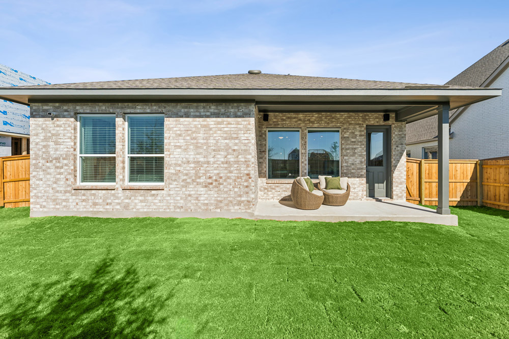 Back view of a brick house with covered patio, two chairs, and fenced yard.
