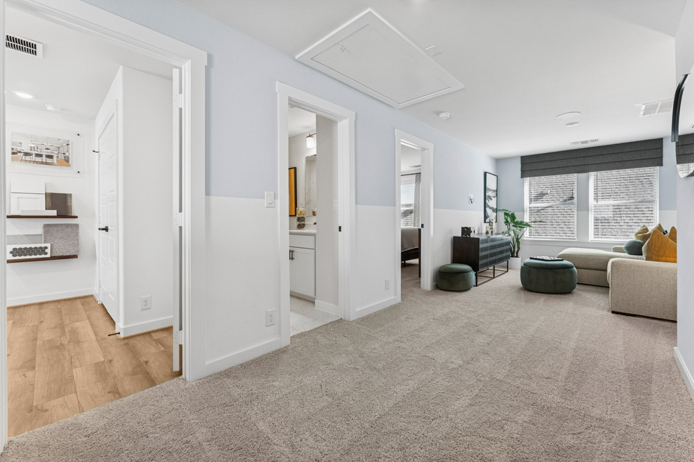 A carpeted hallway with doors to a bathroom and bedroom, leading to a bright living area.