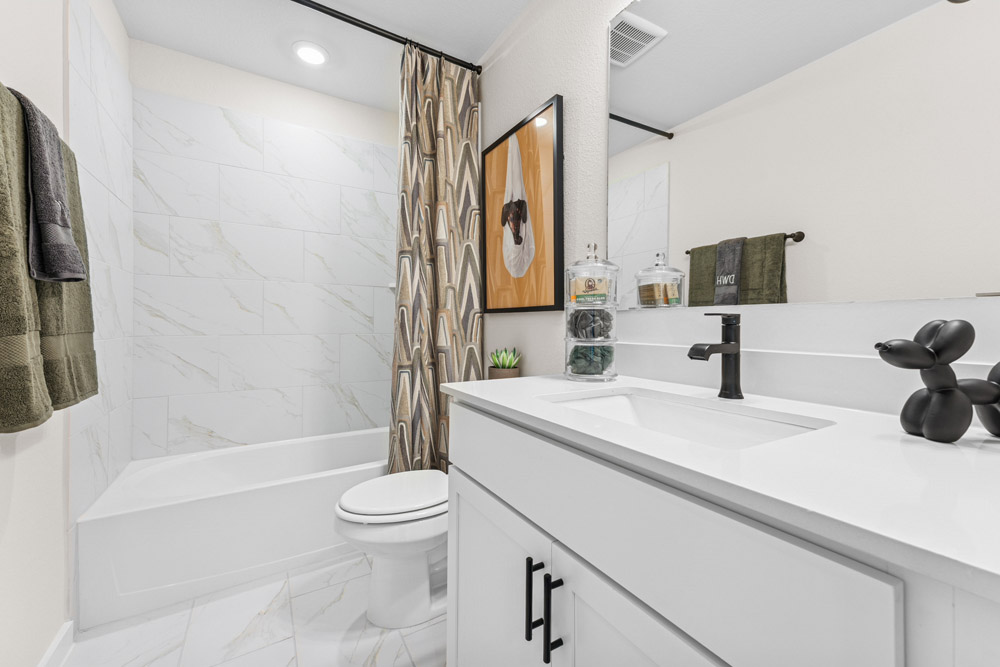 Modern bathroom with white marble tiles, a bathtub, black fixtures, and decorative accents.