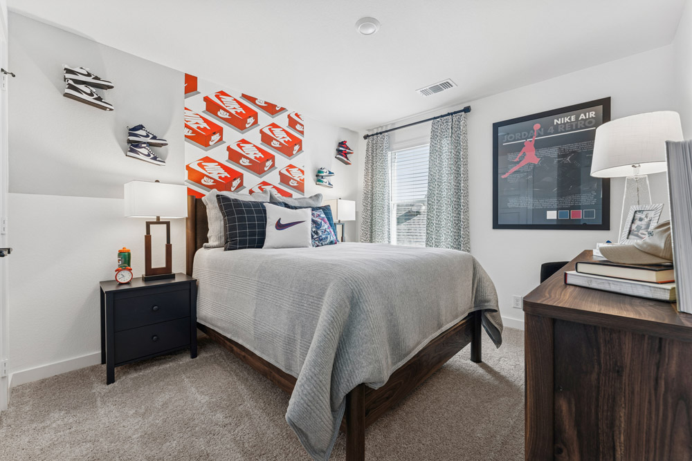 Bedroom with a bed, shoe display on wall, Nike decor, and sunlight coming through window.