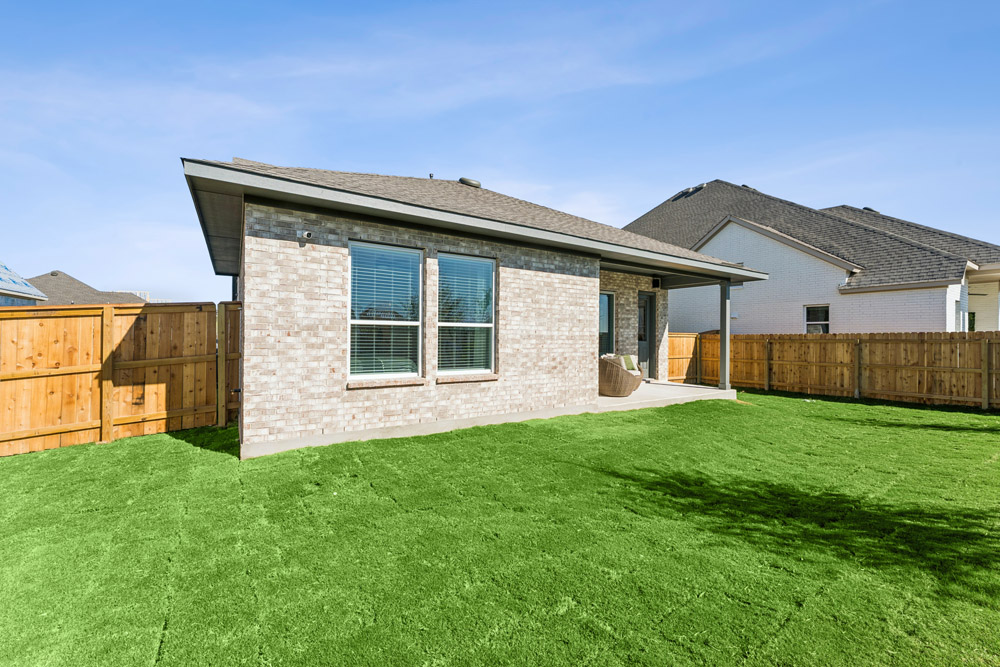 Back view of a brick house with large windows and a fenced backyard with grass.