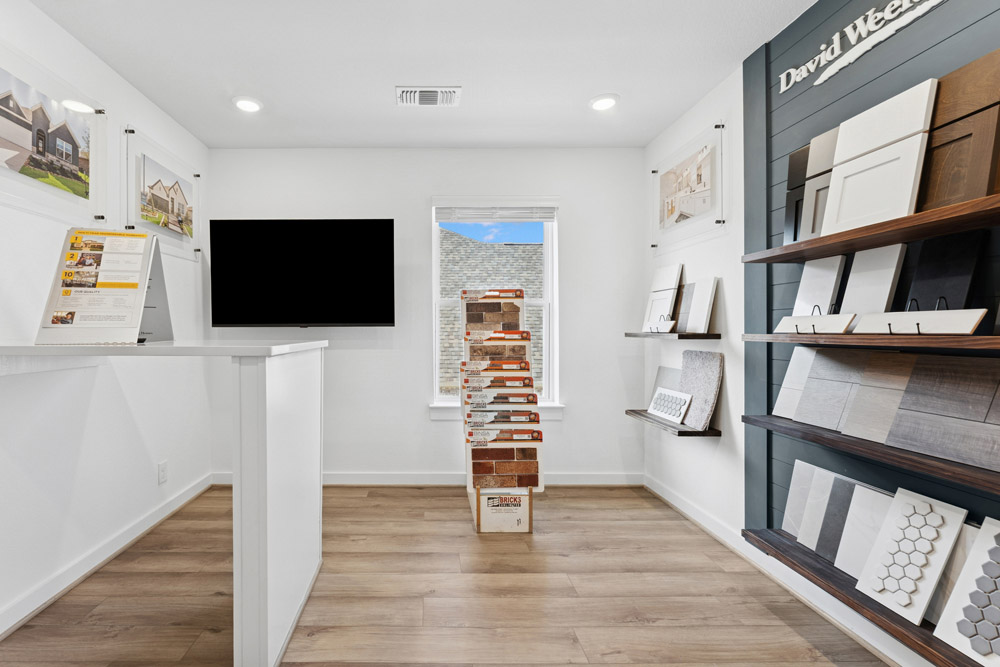 A modern showroom with sample boards, a TV, and a stack of bricks near a window.