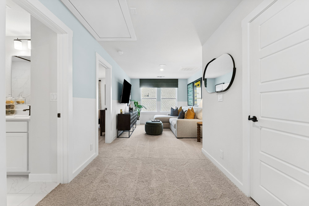 Hallway with beige carpet, leading to a living area with a sofa and wall-mounted TV.