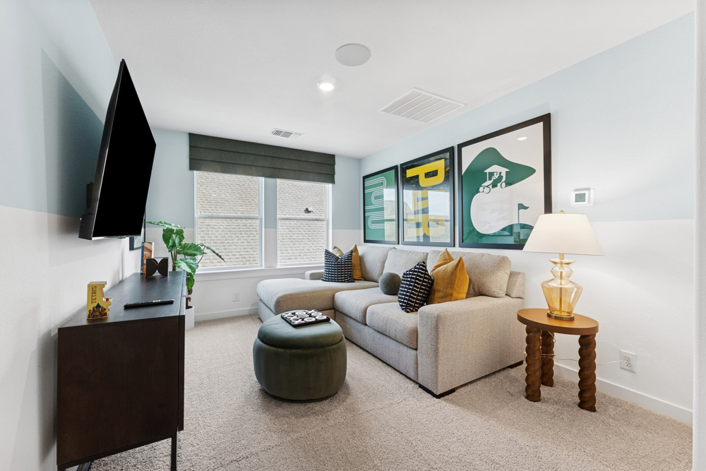 Modern living room with sectional sofa, wall art, TV, ottoman, and side table with lamp.