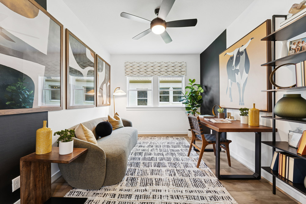 Modern home office with desk, sofa, art on walls, rug, and large window letting in natural light.