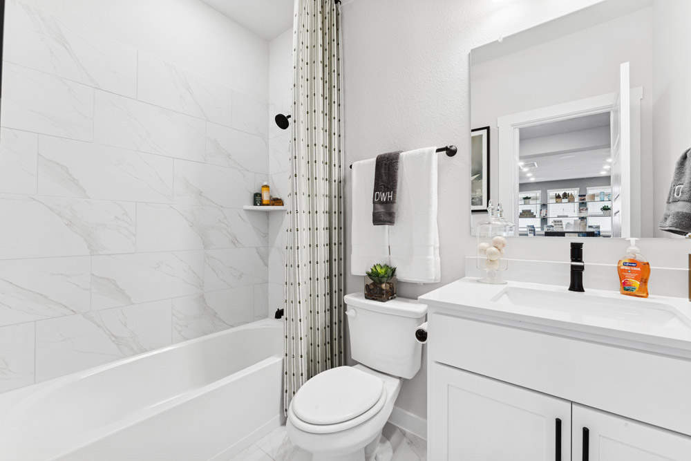 Modern white bathroom with a bathtub, toilet, vanity, and a wall-mounted mirror.