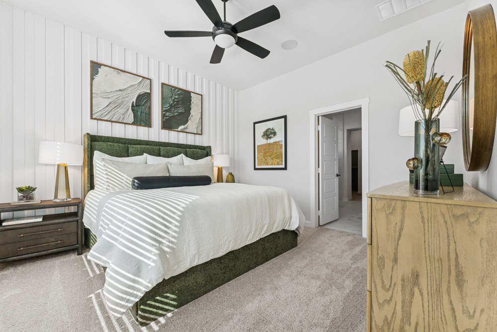 Modern bedroom with green bed, white bedding, wood furniture, and wall art.