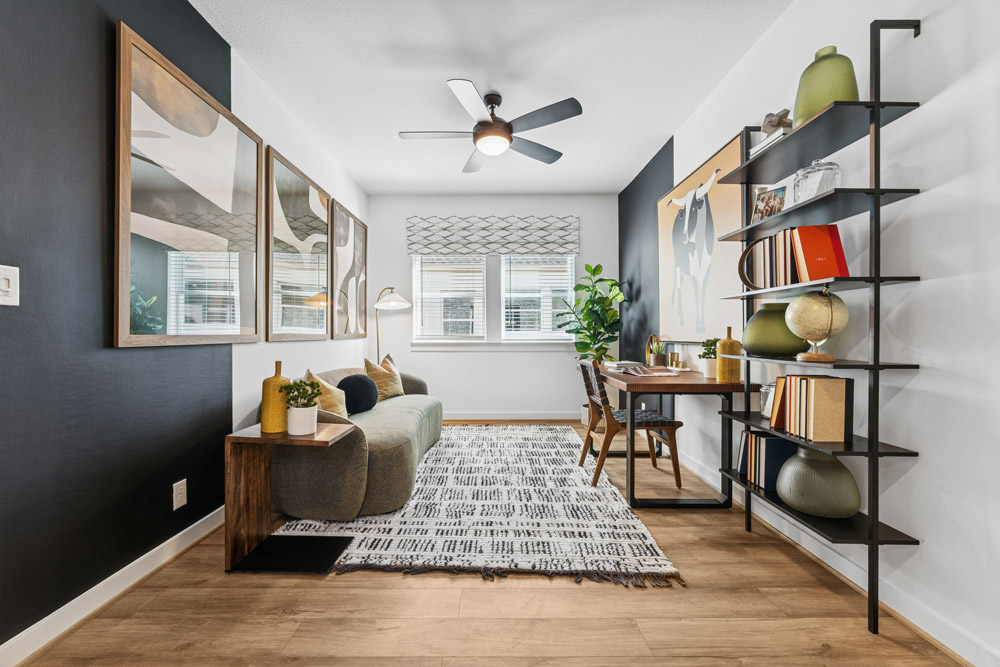 Modern living room with a sofa, desk, shelving unit, and large windows with natural light.