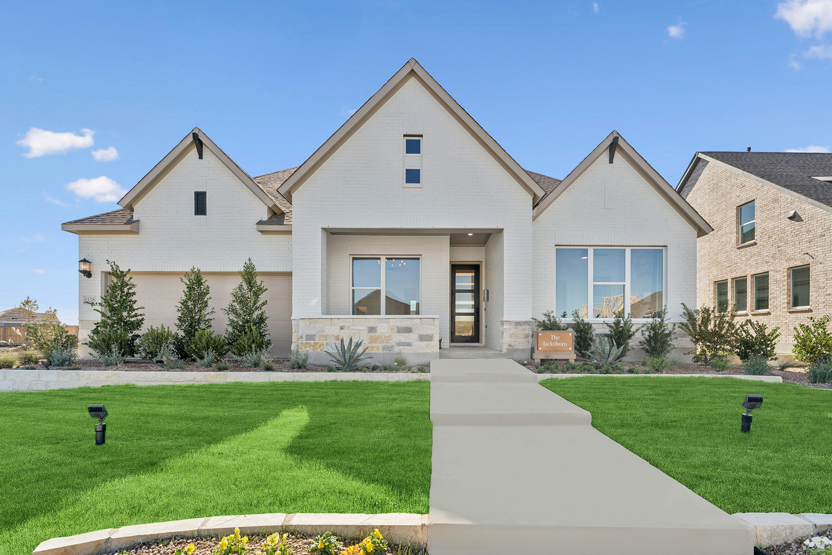 Modern single-story house with white brick exterior, landscaped lawn, and clear blue sky.