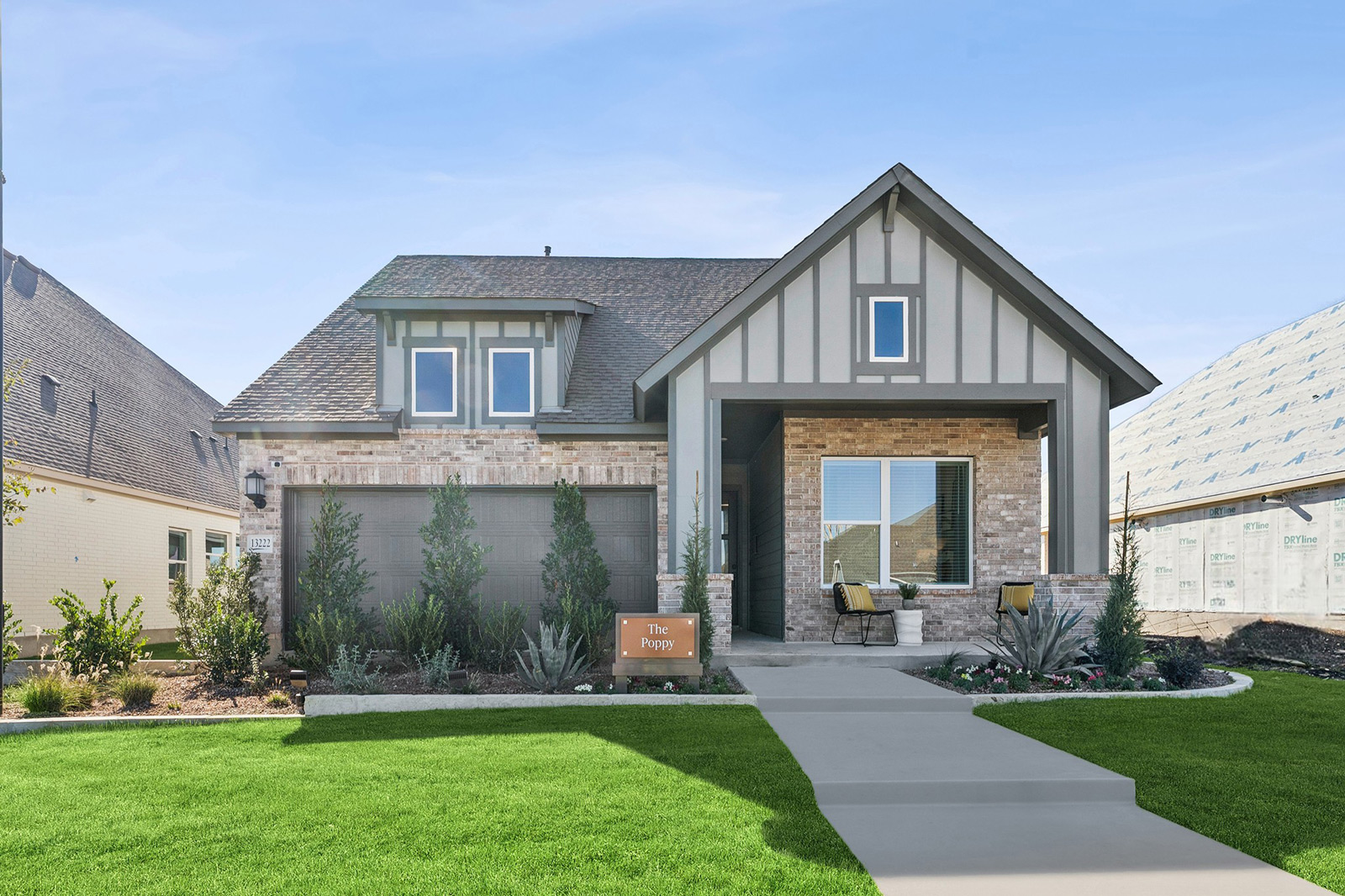 Modern single-story house with gabled roof, front porch, and landscaped yard on a sunny day.