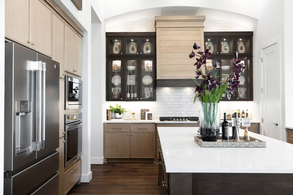 Modern kitchen with stainless steel appliances, marble island, and a vase of dark purple flowers.