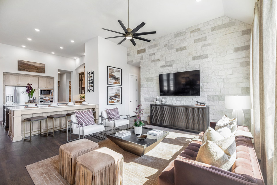 Modern living room with stone accent wall, mounted TV, and open kitchen in the background.