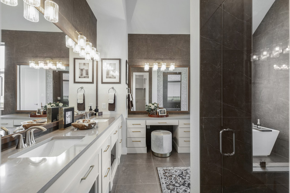 Modern bathroom with double sinks, vanity, glass shower, and large mirrors under bright lights.