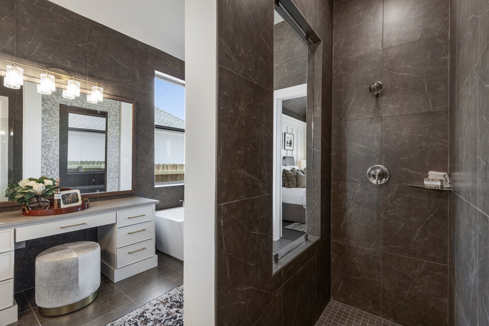 Modern bathroom with dark tiled shower, vanity with stool, and large mirrors.