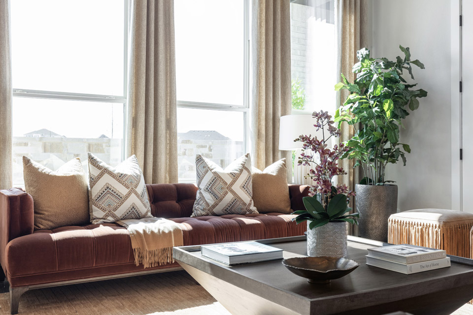 Modern living room with a brown sofa, patterned pillows, plants, and a wooden coffee table.