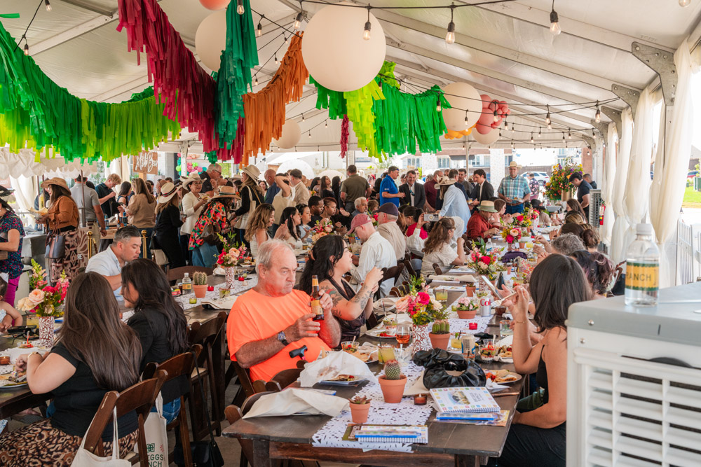 A large group of people dining and socializing under a decorated event tent.