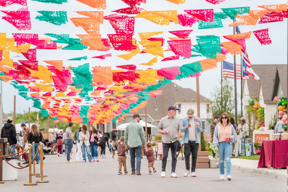 People walk under colorful papel picado banners at an outdoor street festival or market.
