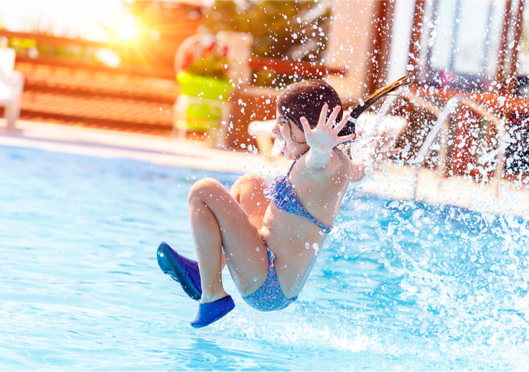 Child in swimsuit splashing into a swimming pool with water droplets in the air.
